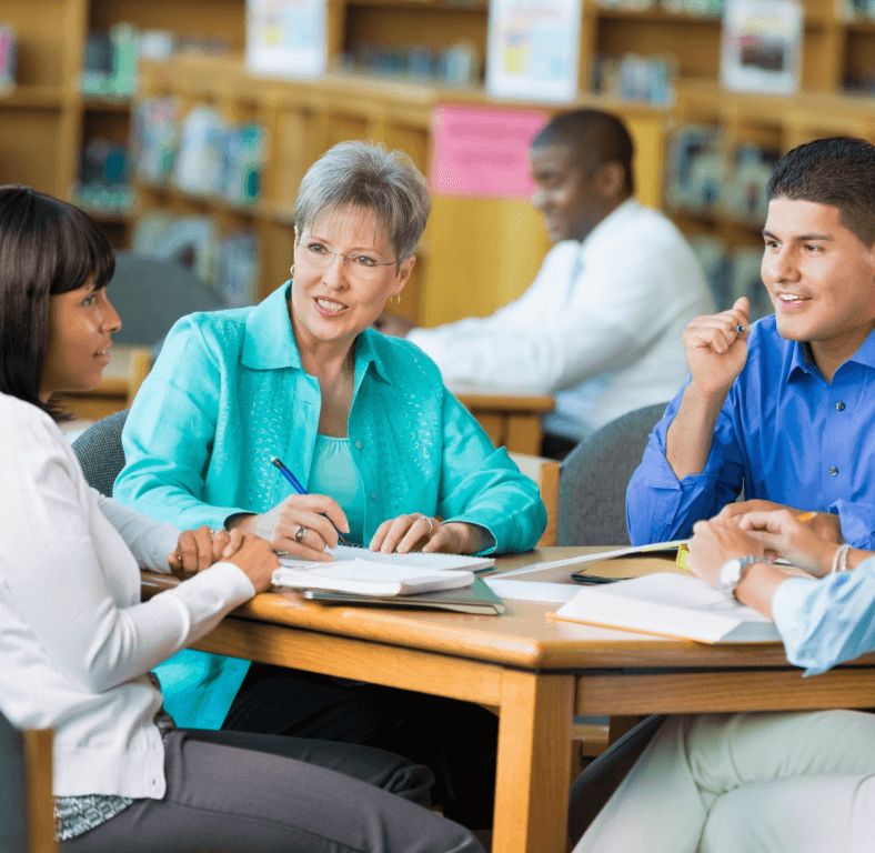 teachers grouped at table with center teacher in bright tourqoiuse blouse