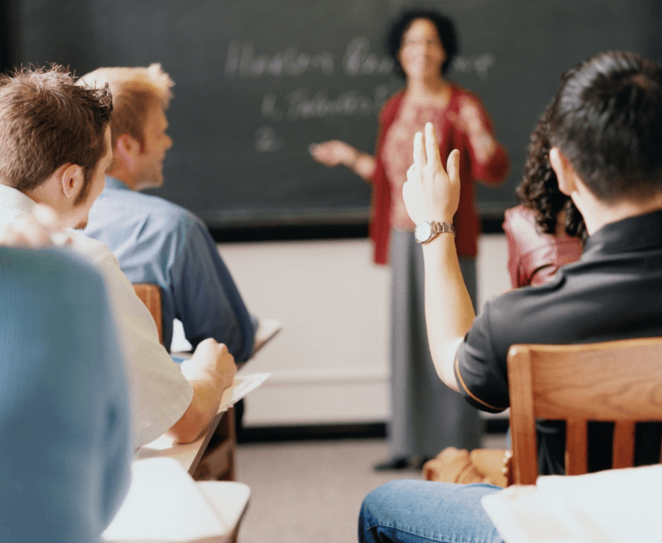 dark-haired instructor with red overlay sweater teaching course at front of room