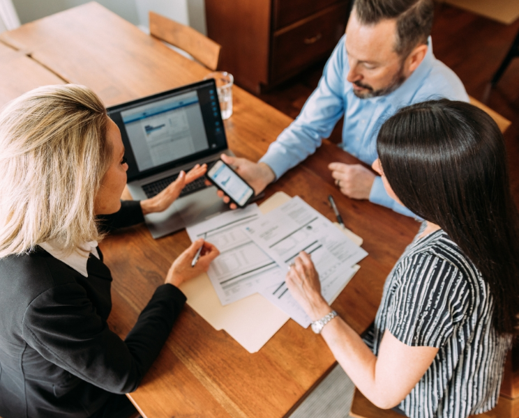 three people at talking at table with documents and laptop